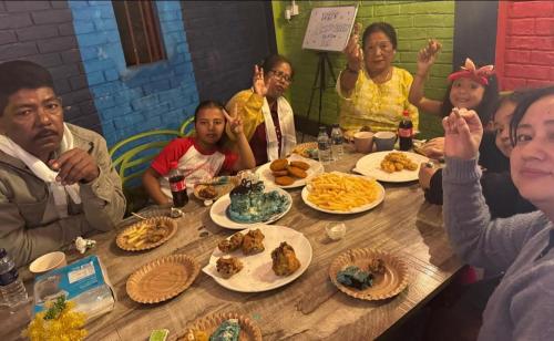 een groep mensen die rond een tafel zitten met eten bij Green Hill Home in Mirik