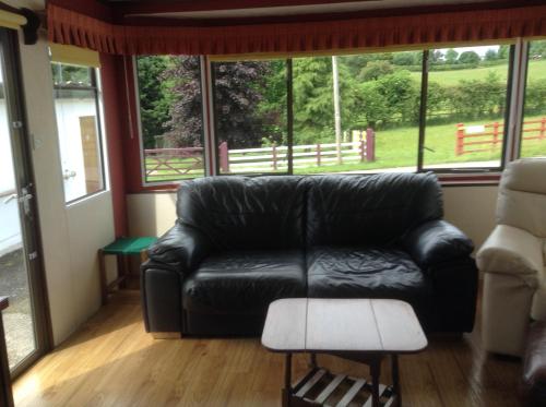 a black leather couch in a living room with windows at Glan Llyn Farm House in Mold