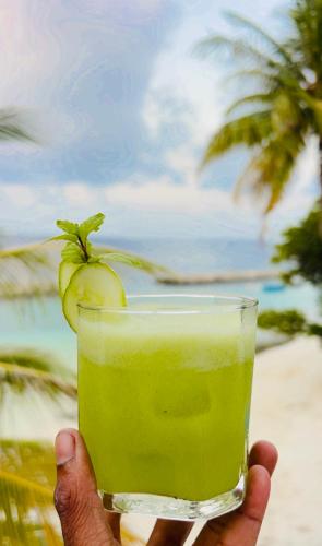 Nautical Nook Maldives في Kendhoo: يد تحمل كوبًا فيه مشروب أخضر مع موزة
