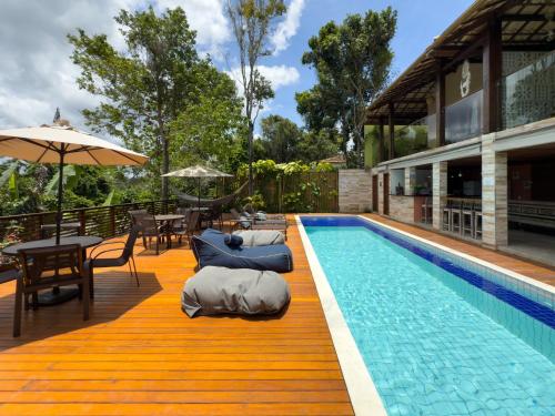 a swimming pool with chairs and an umbrella next to a house at Villa Maritaca Condomínio de 4 Casas de Locação por Temporada de Alto Padrão com SPA in Arraial d'Ajuda