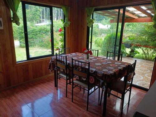 een eetkamer met een tafel, stoelen en ramen bij Cabañas Mis Nietos in Licán Ray