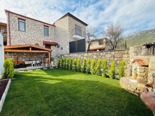een achtertuin met een stenen muur en groen gras bij Kösedere Stone Houses in Karaburun