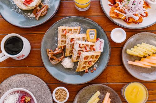 a table topped with plates of waffles and other breakfast foods at Mayan Monkey Los Cabos - Social Hotel in Cabo San Lucas