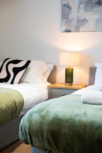 two beds in a room with a lamp on a table at Shenley House- Premium Stay, Private Parking for multiple cars, Sleeps 6, 2 Bedroom, 2 Ensuites, Central MK in Milton Keynes