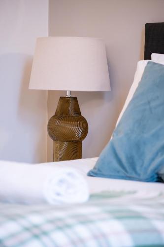 a bed with a lamp next to a blue pillow at Shenley House- Premium Stay, Private Parking for multiple cars, Sleeps 6, 2 Bedroom, 2 Ensuites, Central MK in Milton Keynes