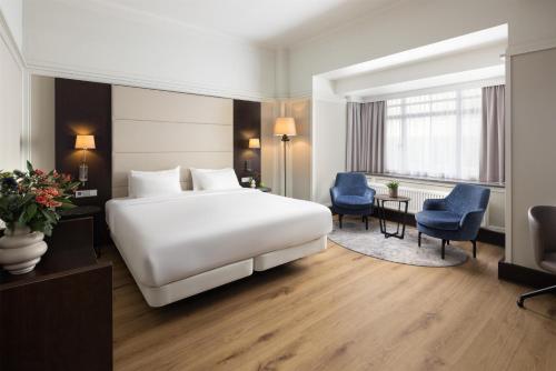 a hotel room with a white bed and blue chairs at NH Atlanta Rotterdam Hotel in Rotterdam
