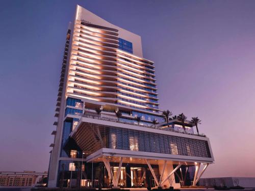 a tall building with palm trees in front of it at Grand Plaza Mövenpick Media City in Dubai