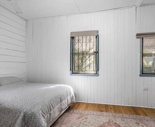 a white bedroom with a bed and two windows at Syntax Cottage in Coalfalls