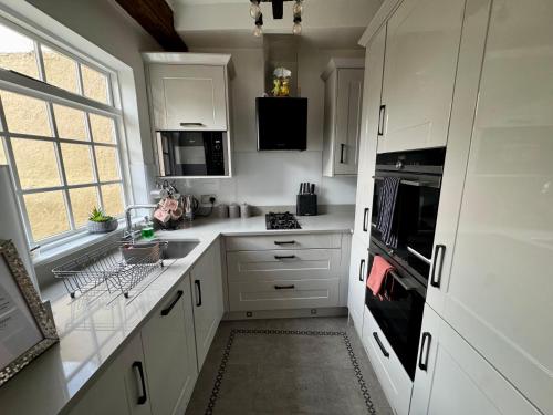 a white kitchen with white cabinets and a window at Castle Yard Cottage in Knaresborough