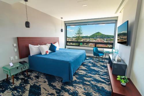 a hotel room with a blue bed and a large window at Hotel Fray Junipero Serra in Tepic