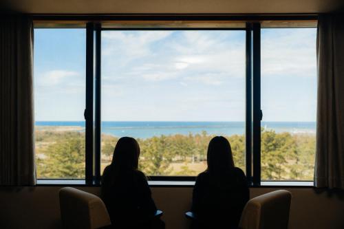 two women sitting in chairs looking out of a window at 9stayリゾートテクノポート福井 in Sakai