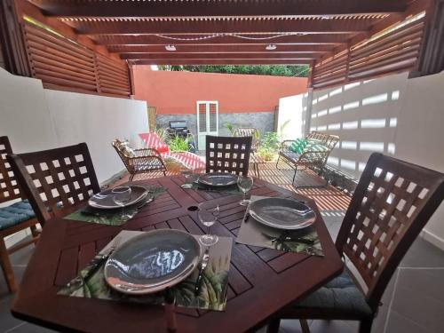 COTTAGE BLUE classé 3 étoiles - 4 à 6 personnes - 2 chambres - accès direct à la plage et à l'esplanade de Boucan Canot avec ses bars et restaurants في سان جيل لي بان: طاولة خشبية مع لوحات وأطباق على الفناء