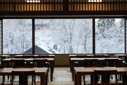 Jozankei Onsen Yurakusoan في Jozankei: غرفة بها طاولات ونافذة كبيرة تطل على أشجار مغطاة بالثلوج