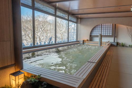 a hot tub in a building with a large window at Jozankei Onsen Yurakusoan in Jozankei