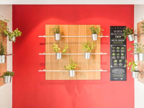 a red wall with potted plants on a shelf at Hotel Ibis Coimbra Centro in Coimbra
