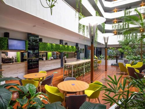 a restaurant with tables and chairs and plants at Novotel Darwin CBD in Darwin