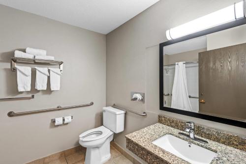 a bathroom with a toilet and a sink and a mirror at Days Inn & Suites by Wyndham Des Moines Airport in Des Moines