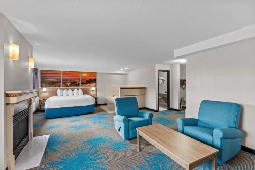 a hotel room with a bed and two blue chairs at Days Inn & Suites by Wyndham Des Moines Airport in Des Moines