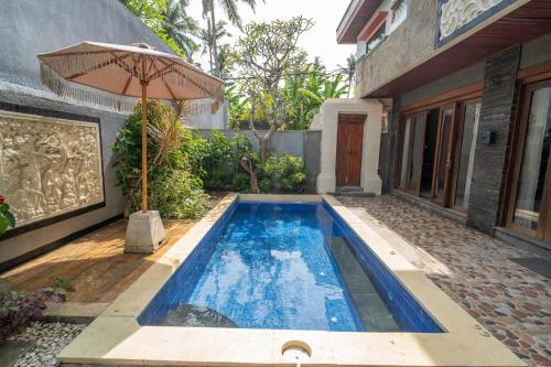 a swimming pool with an umbrella next to a house at Kayangan Saba Villa in Keramas