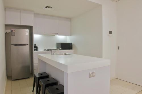 a white kitchen with a counter and a refrigerator at 1BR Waterfront Apartment in Barangaroo with Free Private Parking in Sydney