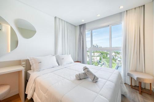 ein weißes Schlafzimmer mit einem Bett und einem Fenster in der Unterkunft Rivieira 2 Suítes e Jacuzzi by Achei Camboriu in Cabeçudas