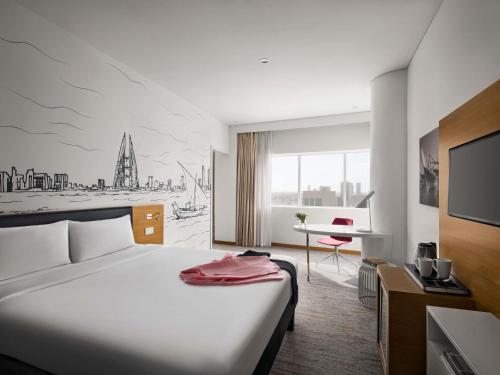 Una habitación de hotel con una cama blanca y un escritorio. en ibis Styles Manama Diplomatic Area, en Manama