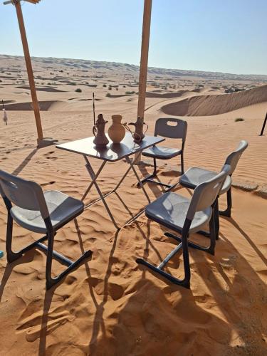 een tafel en stoelen in het zand in de woestijn bij ESCAPE cAMp2 in Badīyah