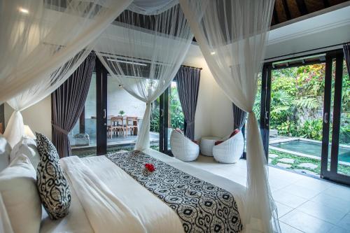 a bedroom with a white bed with curtains and windows at Wardana Ubud Villa I in Ubud