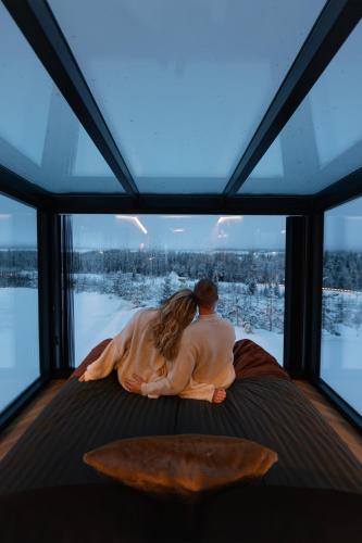 a couple sitting on a bed looking out of a window at Arctic Lumo Resort in Kuusamo