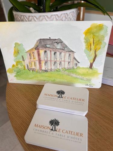 Le CatelierにあるMaison Le Catelierの3枚のカードが置かれたテーブルの上の家の絵
