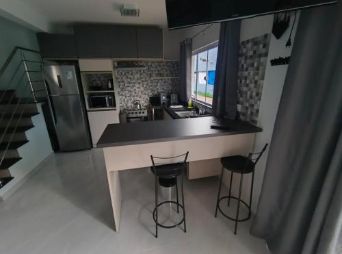 een keuken met een aanrecht en twee barkrukken bij Sobrado 3 Condomínio Sobre as Ondas, 4min a pe da Praia in Guaratuba