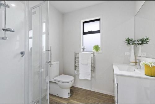 a white bathroom with a toilet and a sink at Sun and fun in the Bay - Home away from Home in Porirua