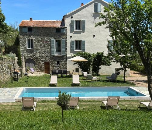 a pool in front of a building with chairs and a house at La demeure des vignes in Murato