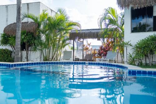 a large swimming pool with palm trees and a building at Oasis Tajaja Pousada Boutique na Costa do Conde in Jacumã