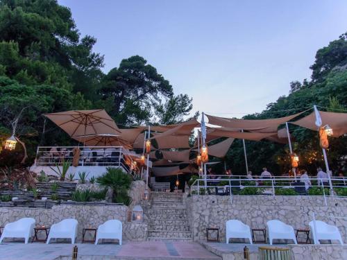 um restaurante com cadeiras brancas, guarda-sóis e pessoas em Baia Delle Zagare - Handwritten Collection em Mattinata