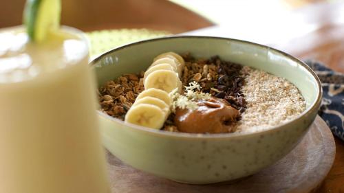 Un tazón de comida con avena y plátanos y un vaso de leche. en Aman Amed Lima 3BR Villa w Panoramic Ocean Views, en Amed