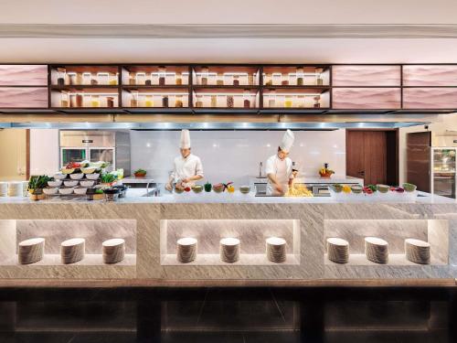 dois chefs preparando comida em uma grande cozinha em Grand Mercure Shenzhen Guangming em Shenzhen