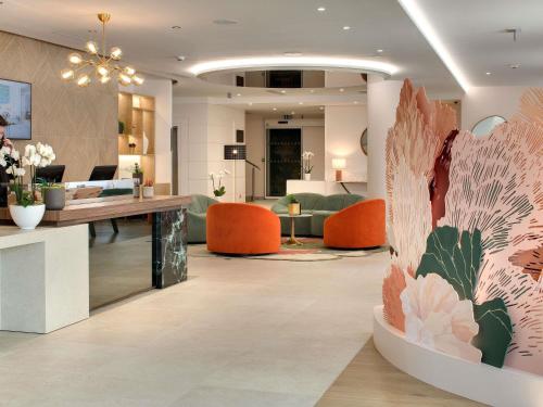 a lobby with a desk and orange chairs at Pullman La Pléiade Montpellier Centre in Montpellier