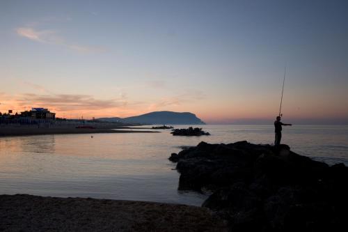 a man fishing on the beach at sunset at Hotel Enzo in Porto Recanati