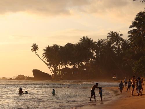 a group of people walking on the beach at sunset at Galawatta Beach Resort in Unawatuna