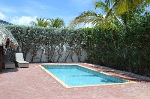 a swimming pool next to a hedge with a palm tree at Tropical villa Curoyal near the beach in Jan Thiel