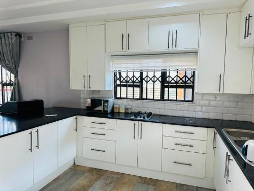 a kitchen with white cabinets and black counter tops at Knovi Guesthouse in Bulawayo