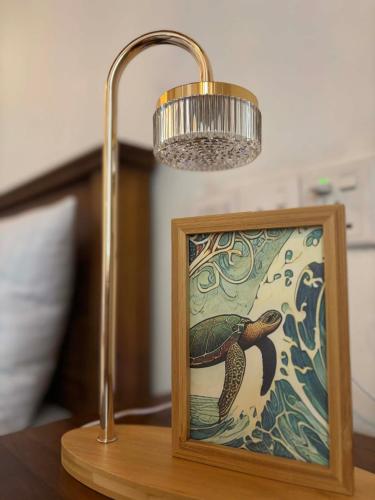 a lamp on a table next to a picture of a turtle at Colonial Surfing Villa Hostel & Home Stay in Midigama East