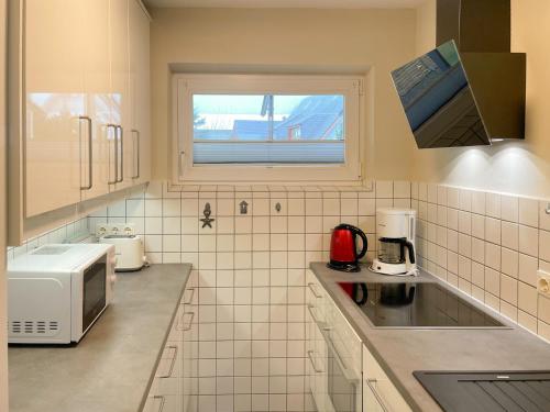 eine weiße Küche mit Mikrowelle und Fenster in der Unterkunft Residenz am Meer Heef in Hörnum