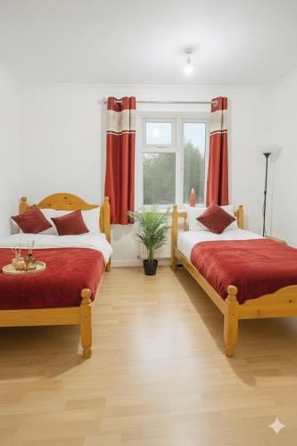 a bedroom with two beds and a window with red curtains at East London Suites in London