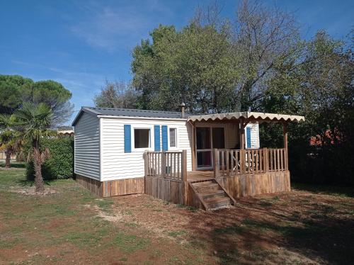 LE FIGUIER mobil home 6 personnes CAMPING LE BEL AIR في Limogne-en-Quercy: كوخ أبيض صغير ذو شرفة وبوابة