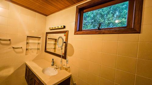 een badkamer met een wastafel, een spiegel en een raam bij Estalagem Entardecer da Serra in Monte Verde