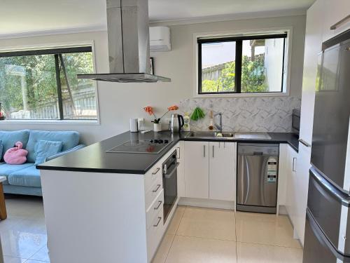 a kitchen with white cabinets and a blue couch at Albany Sunny Deck Retreat in Auckland