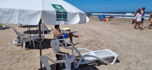 a woman sitting in a chair under an umbrella on the beach at Club carilo playa Edificio del bosque in Carilo