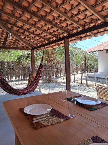 een houten tafel met borden en glazen en hangmatten bij Casa Beleza Atins in Atins